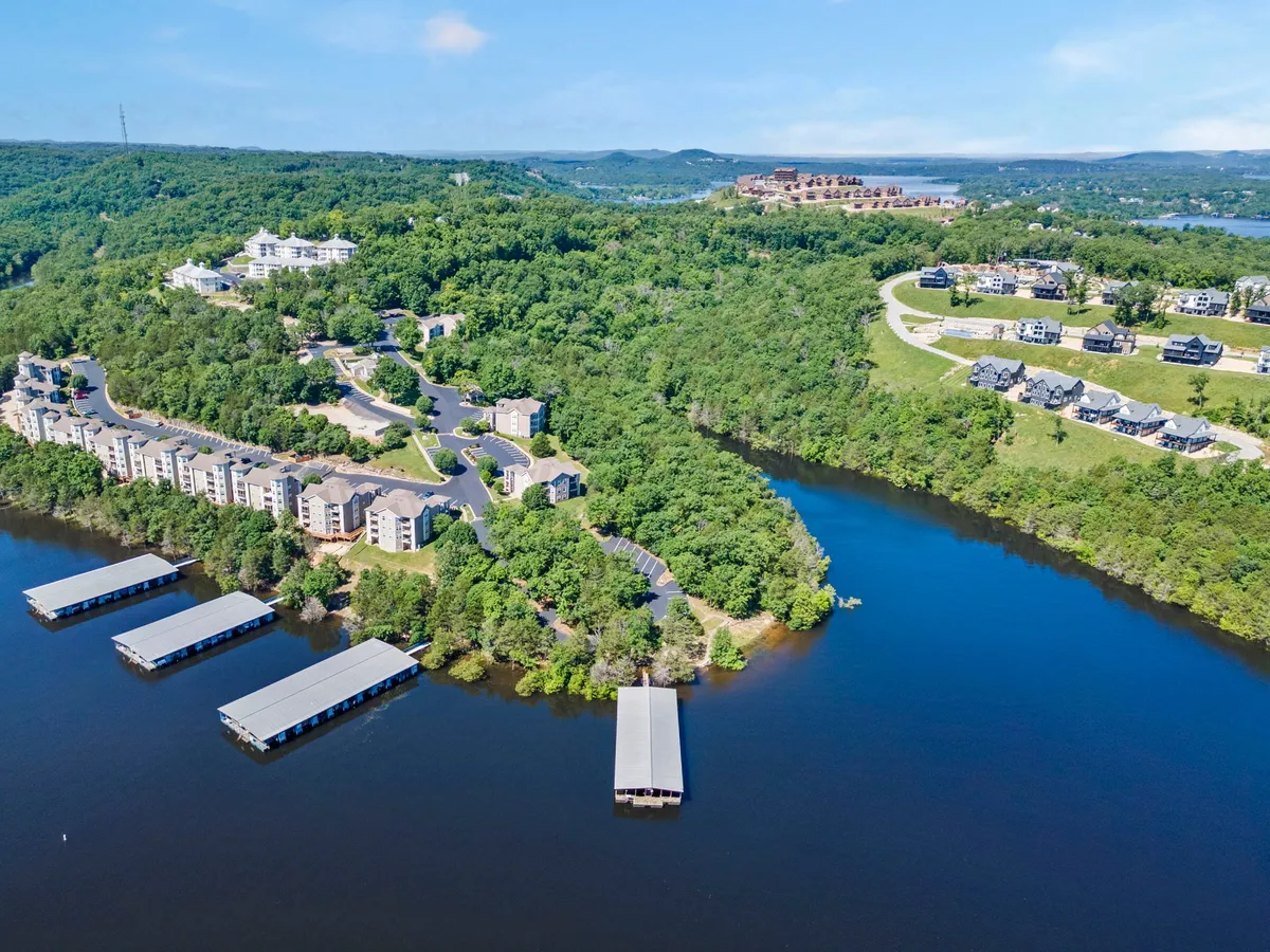 A tranquil waterfront setting featuring docks, residential resort buildings, and abundant greenery. Curved roads wind through the scene, suggesting a leisurely pace and the opportunity for lakeside strolls or community gatherings at sunset. The water shimmers in the background, underscoring the lakeside charm.