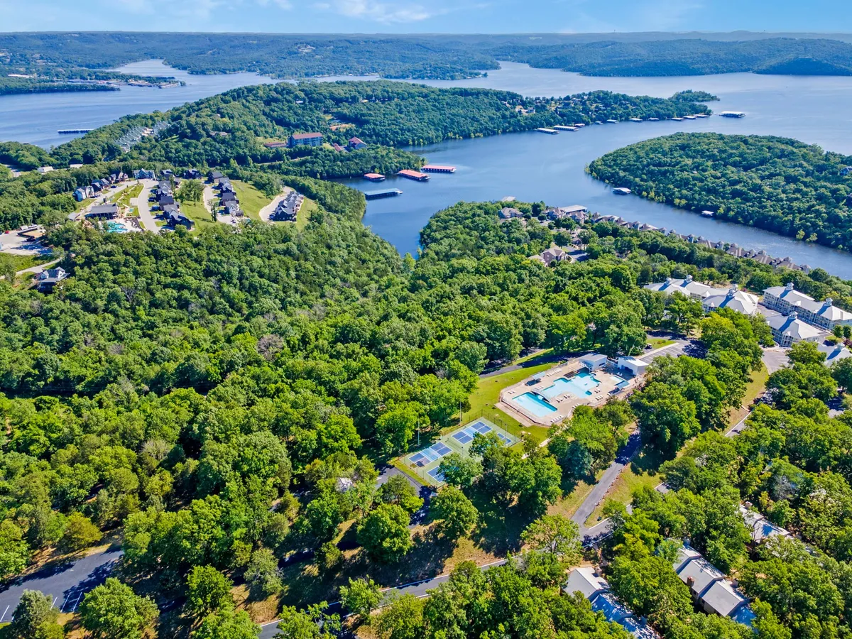 A broad exterior shot capturing a swimming pool, tennis courts, lush greenery, a lake view, and residential buildings. The image blends multiple recreational amenities and showcases the natural surroundings, suggesting both relaxation and activity.