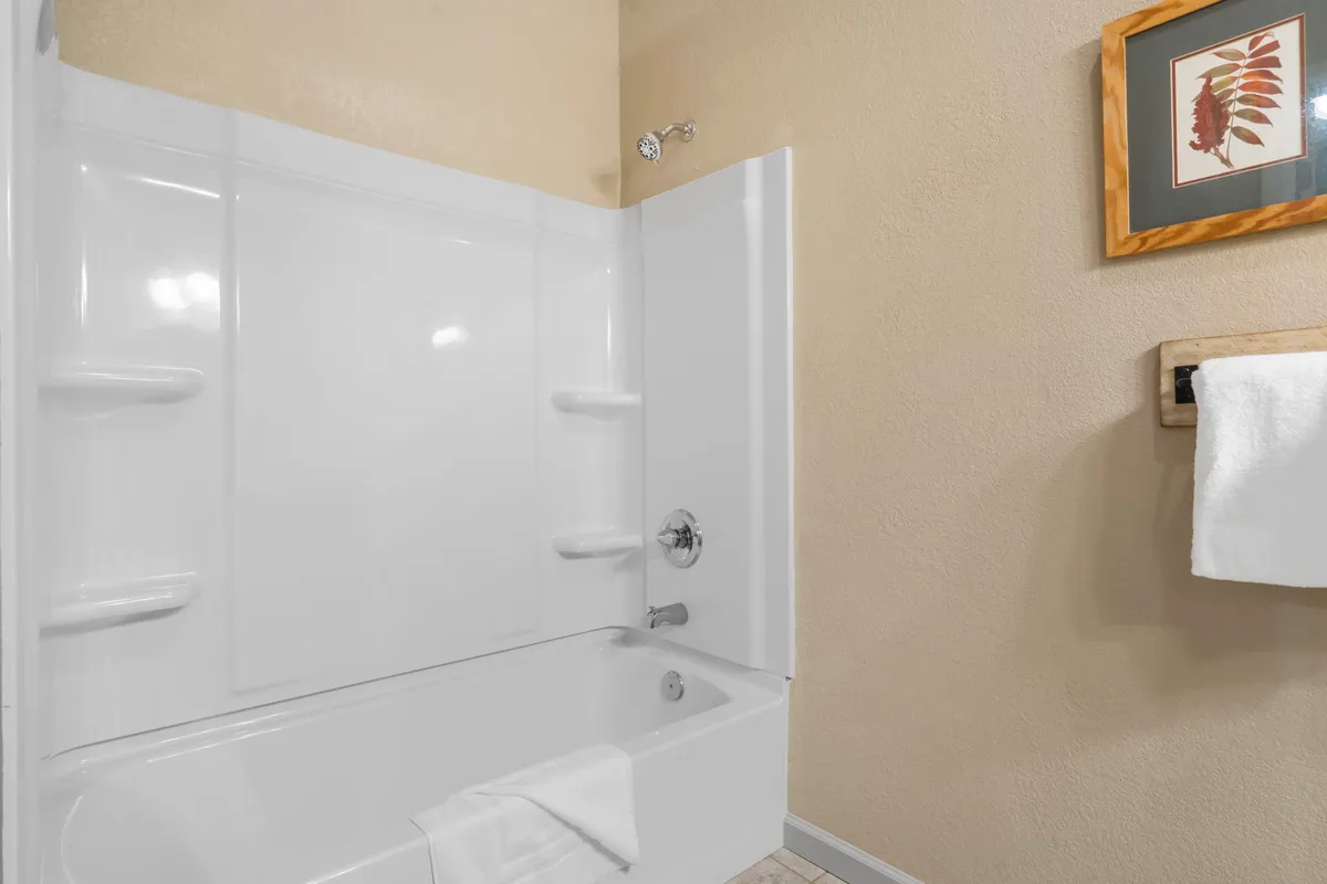 A serene bathroom scene featuring a deep soaking bathtub, a towel rack with fresh towels, and framed artwork on the wall. The setting is calm and spa-like, inviting guests to unwind and refresh after a day of adventure.
