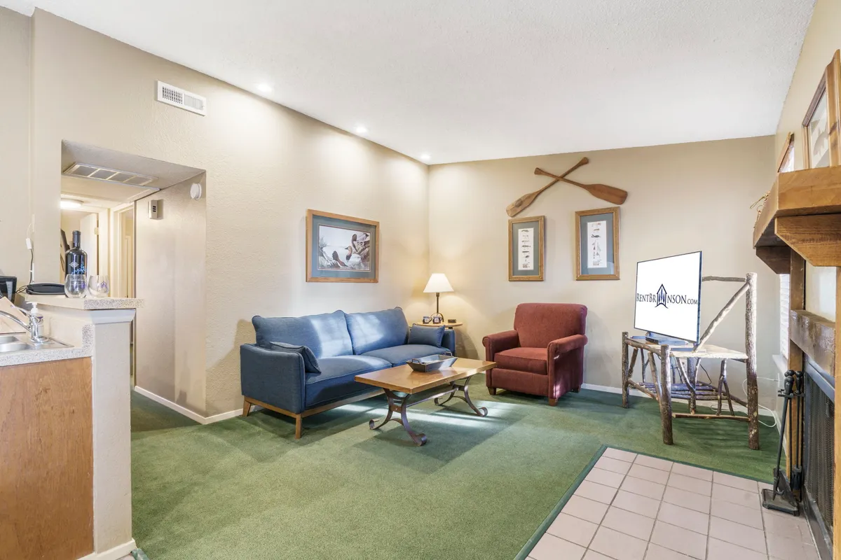 The image showcases a bright, inviting living area with a plush blue sofa and a bold red armchair gathered around a cozy coffee table. Framed artwork adorns the walls, and a warm lamp casts a welcoming glow, creating a comfortable space ideal for relaxing, reading, or socializing with loved ones.