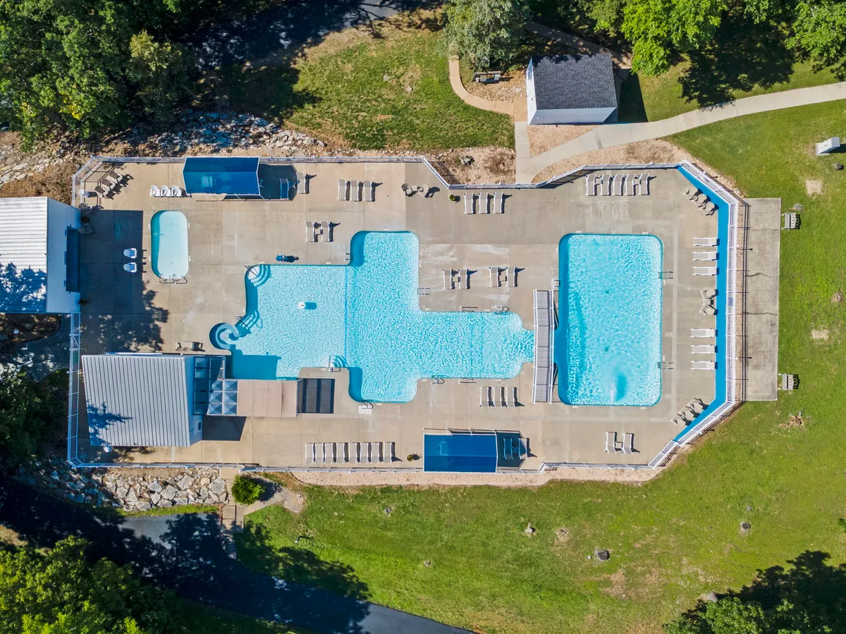 A bright, inviting pool area with swimming pools, deck chairs, and surrounding greenery, set close to a poolside building. The area looks peaceful, ideal for both active and relaxed outdoor activities.