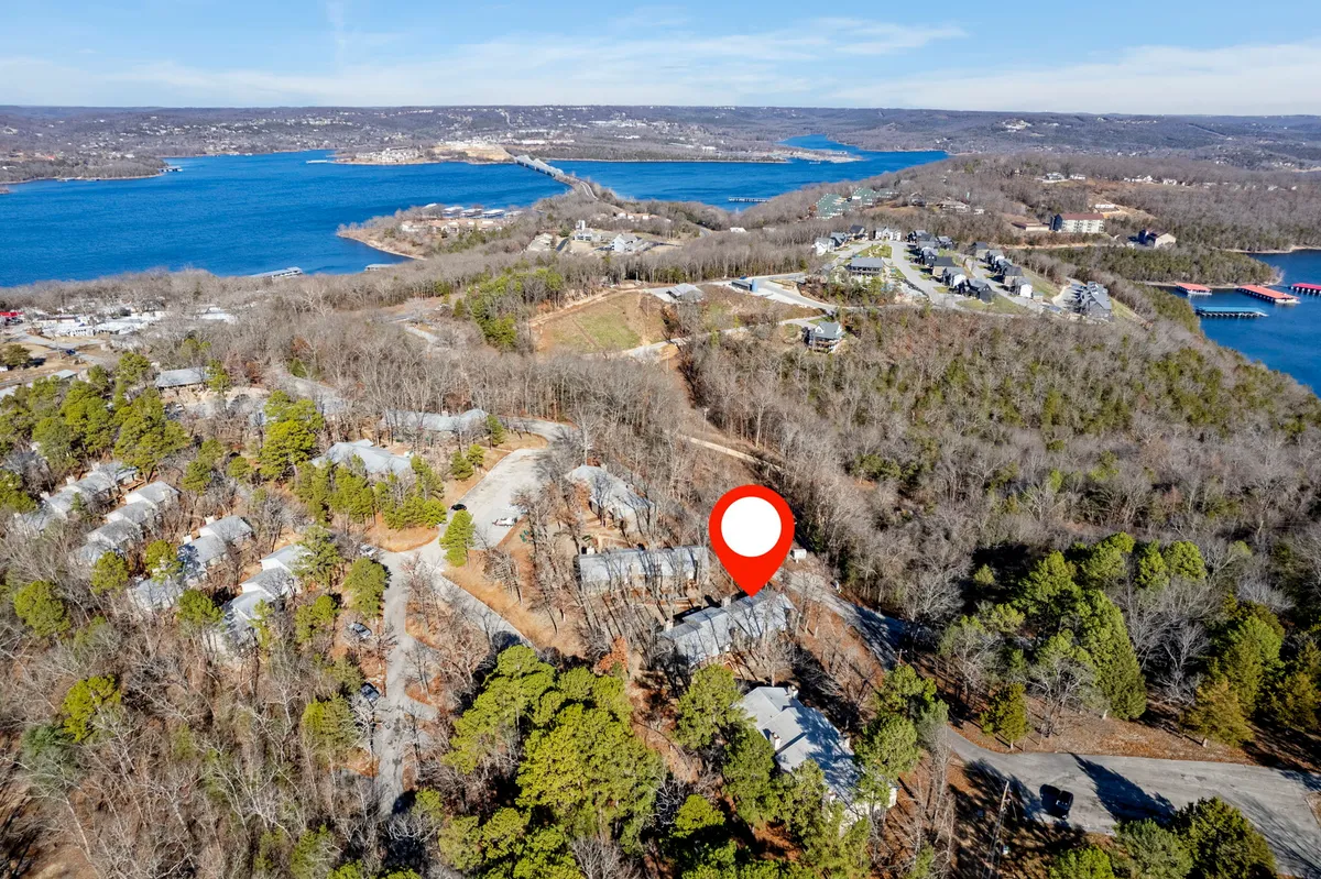 A cluster of buildings bordering a scenic water body, framed by a tree line and intersected by roadways. The setting is tranquil and showcases easy access to both nature and water, reinforcing opportunities for walks, wildlife observation, and outdoor exploration with pets.