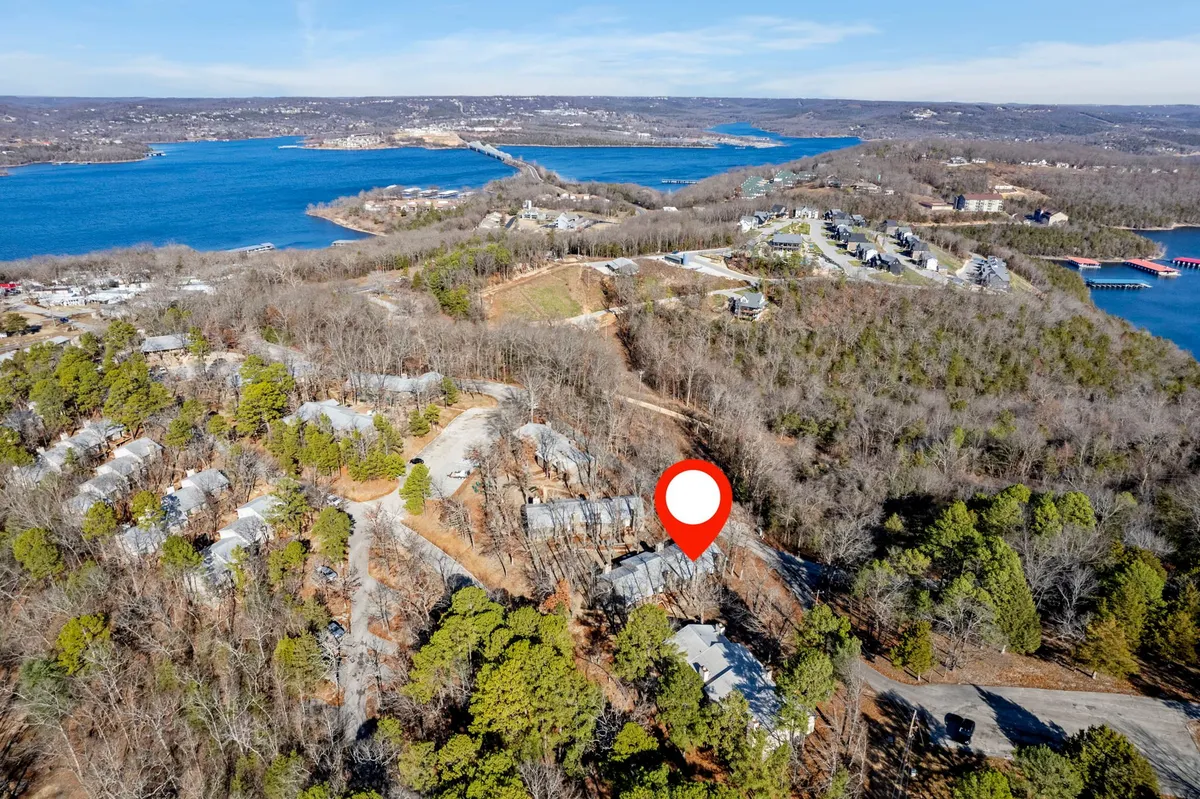 A tranquil scene overlooking a lake, with a wooded area and residential buildings in the background. The expansive natural setting suggests opportunities for hiking, leisurely walks, and exploring local flora and fauna, all in a serene lakeside environment.