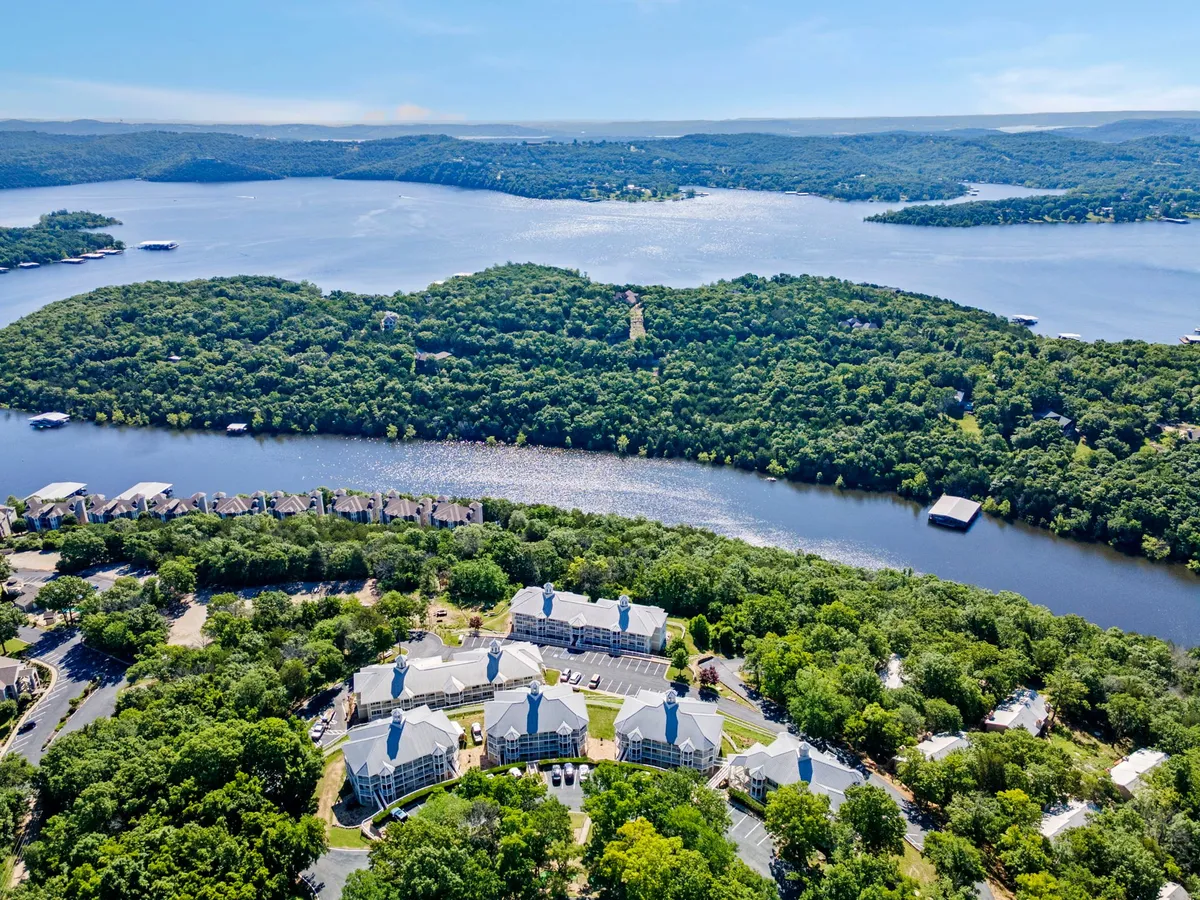 A wide view overlooking Table Rock Lake, showcasing the shimmering water, encircling hills, and nearby residential buildings nestled among the trees. The expansive vista hints at opportunities for swimming, kayaking, or exploring coves.