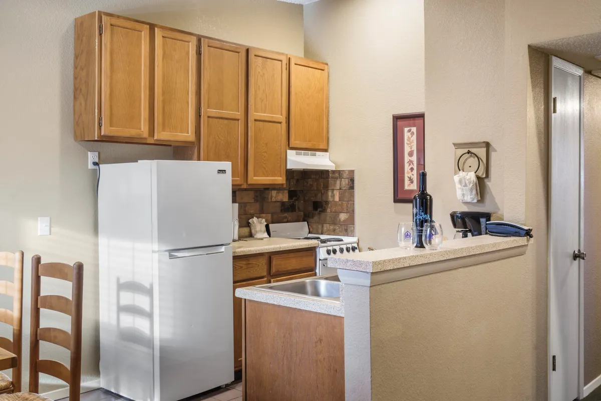A cozy and functional kitchen setup with a white refrigerator, wooden cabinetry, a stove, and ample counter space. The decorative wall art adds a homey touch to the modern appliances.