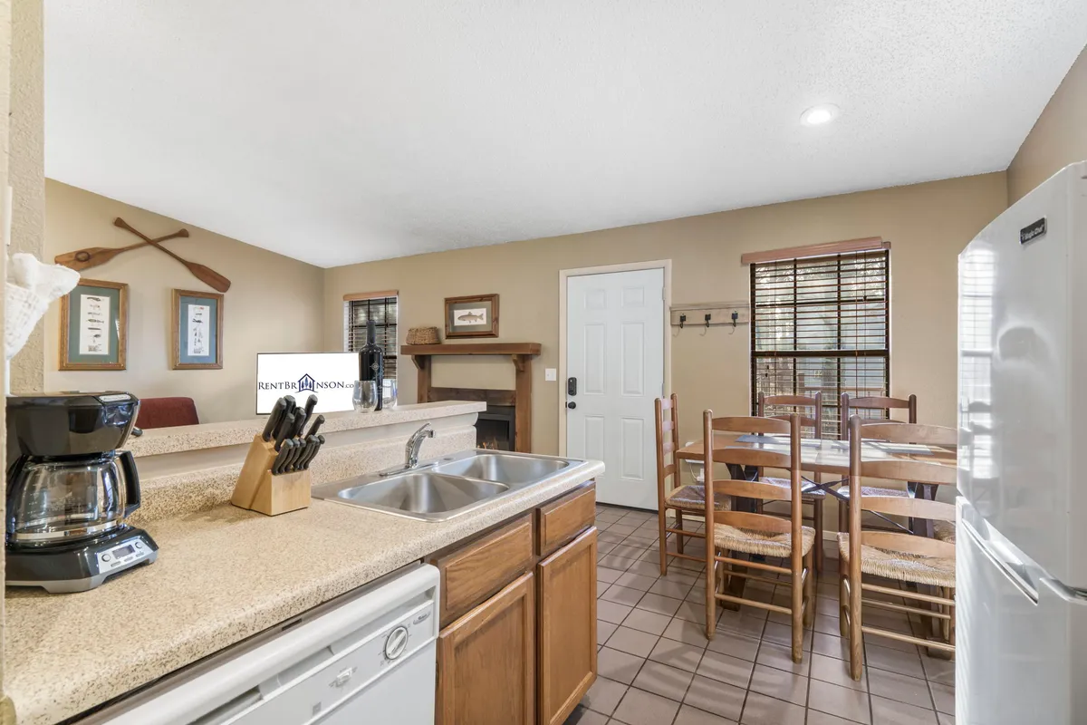 A warm, open-concept kitchen featuring a center island with a sink, a dining table set for a meal, a coffee maker, and inviting wall decorations. The arrangement highlights both the kitchen and dining area in a single view, emphasizing togetherness and functionality.